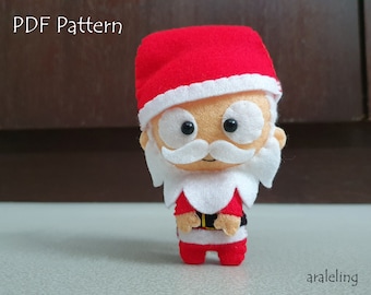 May include: A felt Santa Claus ornament with a red hat, white beard, and black eyes. The ornament is standing on a white surface. The text "PDF Pattern" is visible in the background.