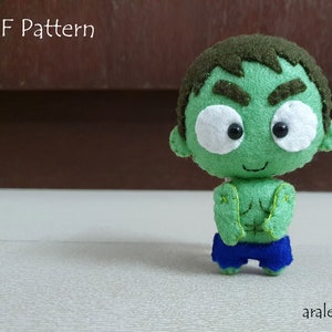 May include: A green felt plush toy of the Hulk character with a brown felt head, white felt eyes, and a black felt mouth. The toy is wearing blue felt shorts. The text "PDF Pattern" is visible in the background.