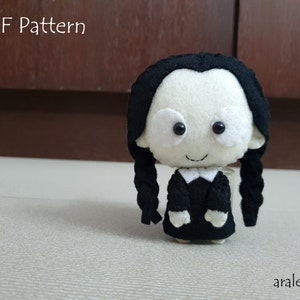 May include: A felt doll of a girl with black hair in braids, wearing a black dress with a white collar. The doll has a white face with black eyes and a small smile.