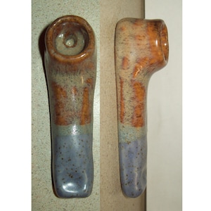 May include: A ceramic pipe with a brown and blue glaze. The pipe has a round bowl and a long, curved stem.