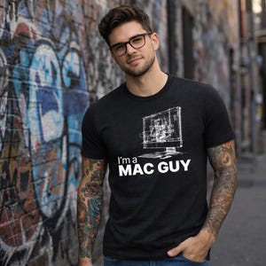 Op de afbeelding: Donkergrijs t-shirt met de tekst "I'm a MAC GUY" en een witte afbeelding van een computermonitor. Het t-shirt heeft een ronde hals.
