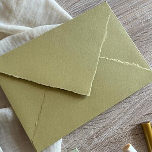 May include: A green envelope with a textured, handmade paper finish. The envelope has a flap with a jagged edge.