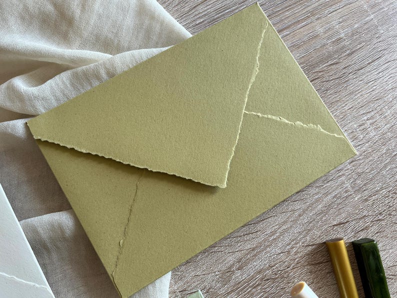May include: A green envelope with a textured, handmade paper finish. The envelope has a flap with a jagged edge.