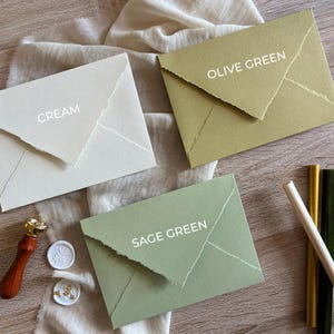 May include: Three envelopes in different colors: cream, sage green, and olive green. Each envelope has a flap with a decorative edge and the color name is written in white text on the front.