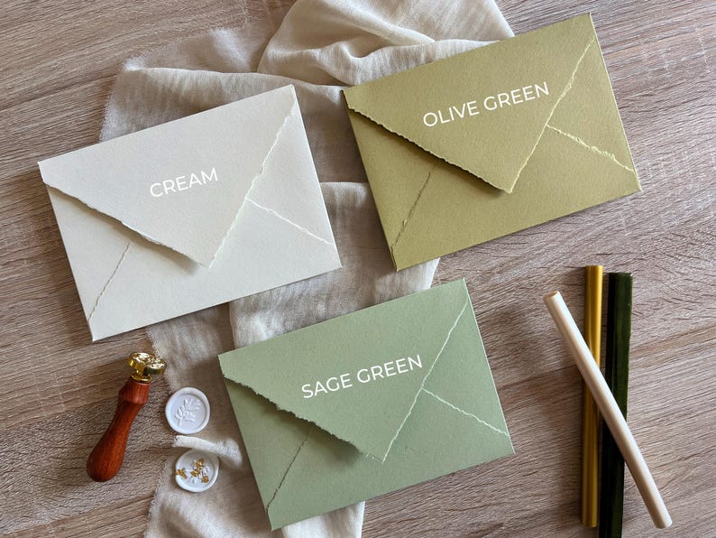 May include: Three envelopes in different colors: cream, sage green, and olive green. Each envelope has a flap with a decorative edge and the color name is written in white text on the front.