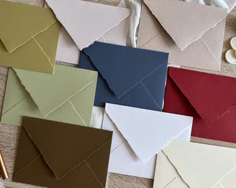 May include: A selection of handmade paper envelopes in shades like olive, navy, and burgundy. The envelopes have a textured finish and torn edges, giving a rustic, artisanal feel. Suitable for stationery or invitations, these envelopes are a unique choice.