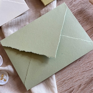 May include: A light green envelope with a textured, handmade paper finish. The envelope is folded in half and has a slightly irregular edge.