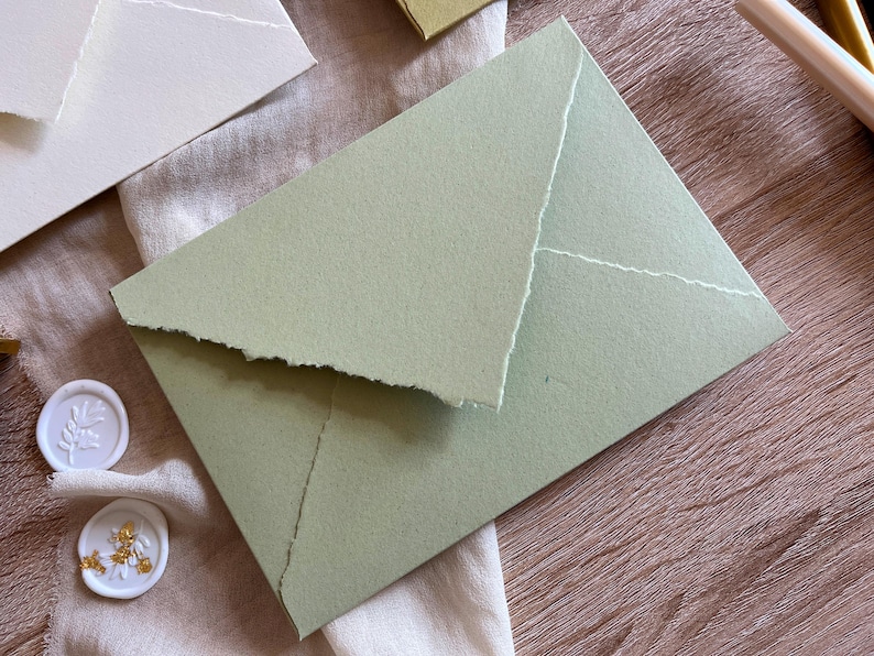 May include: A light green envelope with a textured, handmade paper finish. The envelope is folded in half and has a slightly irregular edge.