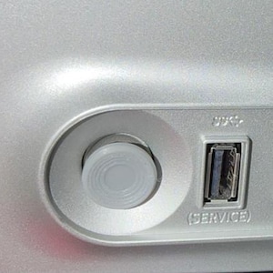 Peut inclure: Un panneau de châssis d'ordinateur argenté doté d'un bouton d'alimentation circulaire, d'un port USB marqué SERVICE, d'un port USB 3.0 bleu marqué PC, d'un port USB supplémentaire, d'une prise casque et d'une entrée d'alimentation alignés.