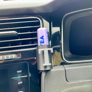 Pu&ograve; includere: Un porta cellulare nero per la ventilazione dell'auto con un balsamo per labbra viola all'interno. Il supporto ha la lettera "T" stampata su di esso.