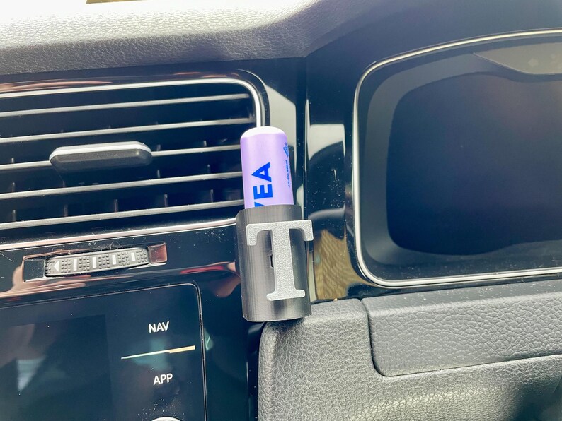 Pu&ograve; includere: Un porta cellulare nero per la ventilazione dell'auto con un balsamo per labbra viola all'interno. Il supporto ha la lettera "T" stampata su di esso.