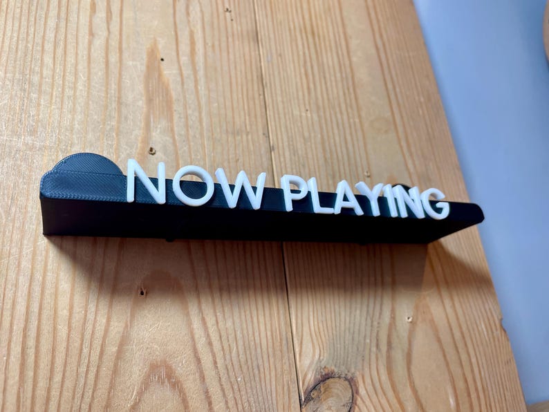 May include: A black sign with white letters that reads "NOW PLAYING".