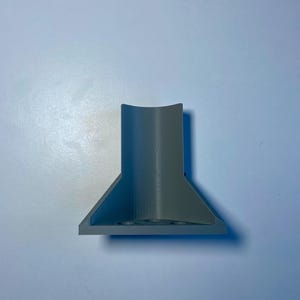 May include: A gray plastic 3D printed object with a cylindrical top and a triangular base.