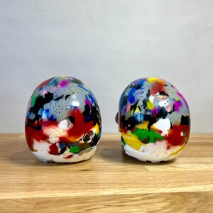 May include: Two colourful, hand-painted ceramic skulls with a glossy finish. The skulls are decorated with a variety of colours, including red, blue, green, yellow, and black.