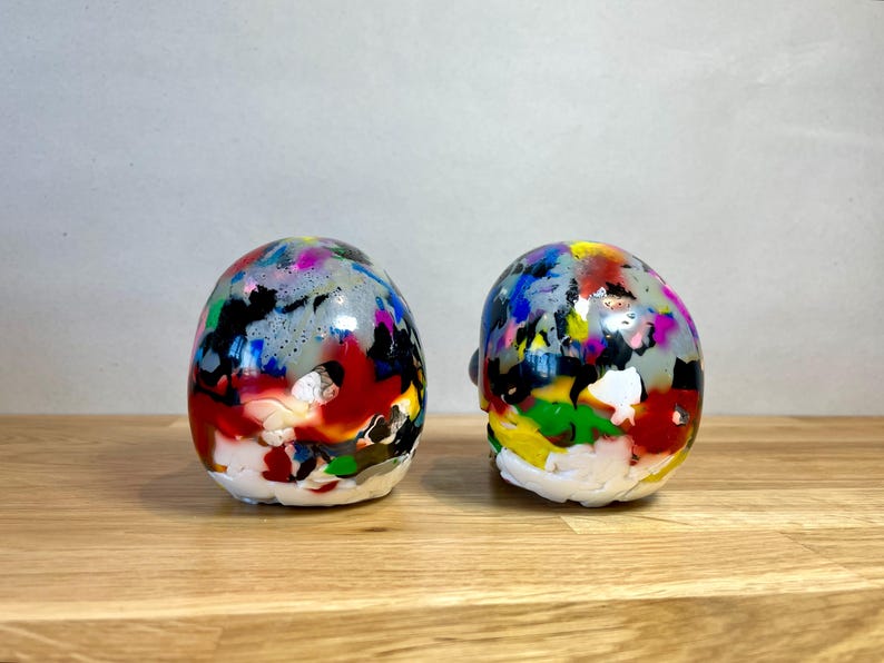 May include: Two colourful, hand-painted ceramic skulls with a glossy finish. The skulls are decorated with a variety of colours, including red, blue, green, yellow, and black.