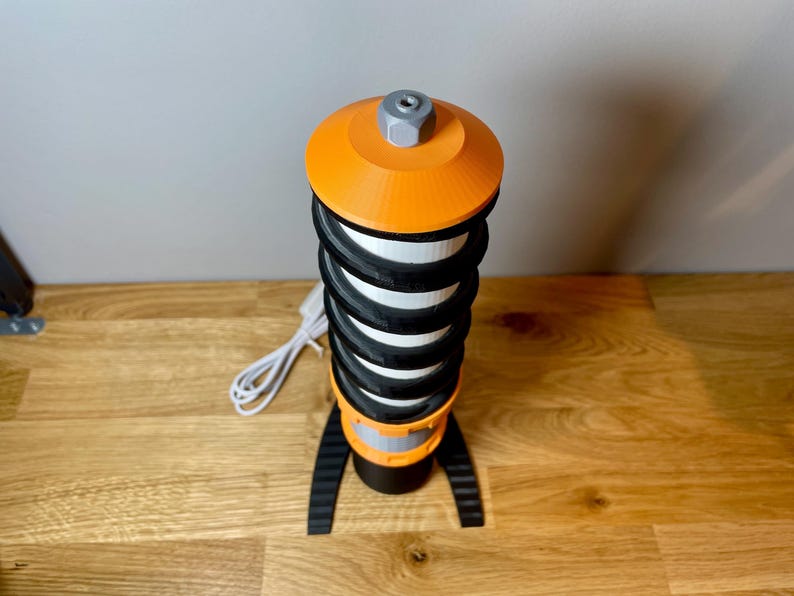 Op de afbeelding: Een zwart-oranje 3D-geprinte lamp met een spiraalvormig ontwerp en een wit snoer.