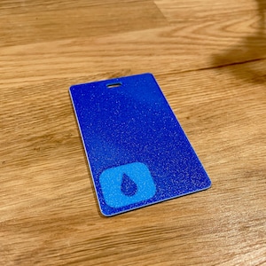 May include: A blue plastic card with a white water drop logo in the center. The card has a hole in the top corner for hanging.