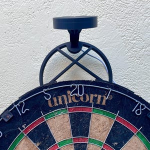 Dart board with attached lamp on the top. The lamp extends out in front of the board in order to cast light on the play area. Lamp is black modern design with a puck light at the end.