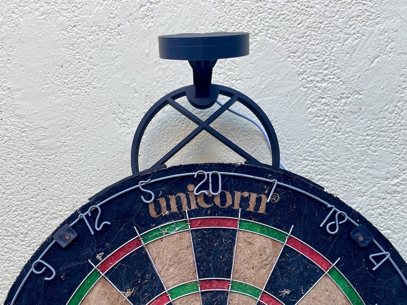 Dart board with attached lamp on the top. The lamp extends out in front of the board in order to cast light on the play area. Lamp is black modern design with a puck light at the end.