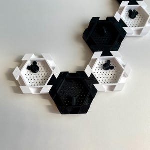 May include: A series of black and white hexagonal wall shelves. Each shelf has a perforated base and a black Mickey Mouse head silhouette. The shelves are arranged in a connected pattern, creating a modern, geometric design.