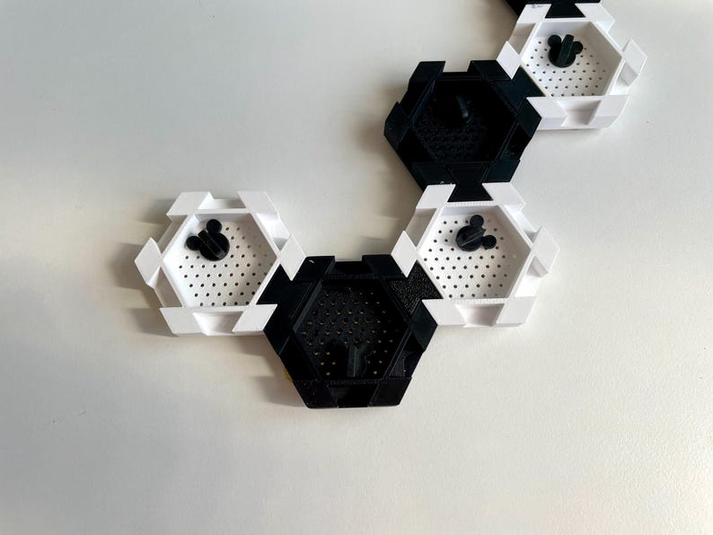 May include: A series of black and white hexagonal wall shelves. Each shelf has a perforated base and a black Mickey Mouse head silhouette. The shelves are arranged in a connected pattern, creating a modern, geometric design.