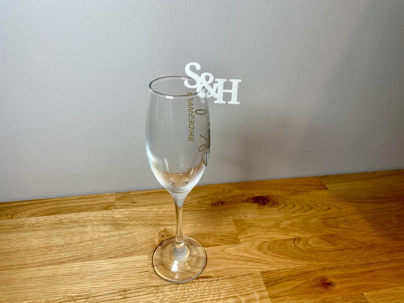 Champagne flute with a set of initial letters clipped onto the side. Drink topper is white and the photo shows a grey background.