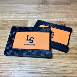 May include: Two black card holders with orange inserts. The top card holder has a carbon fiber pattern. The bottom card holder has a geometric pattern and the text "LS LAYEREDSHAPE".