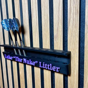 Puede incluir: Soporte negro para dardos con tres dardos. Los dardos tienen ca&ntilde;as negras y plumas Power azules y blancas. El soporte tiene el texto "Luke "The Nuke" Littler" en morado.