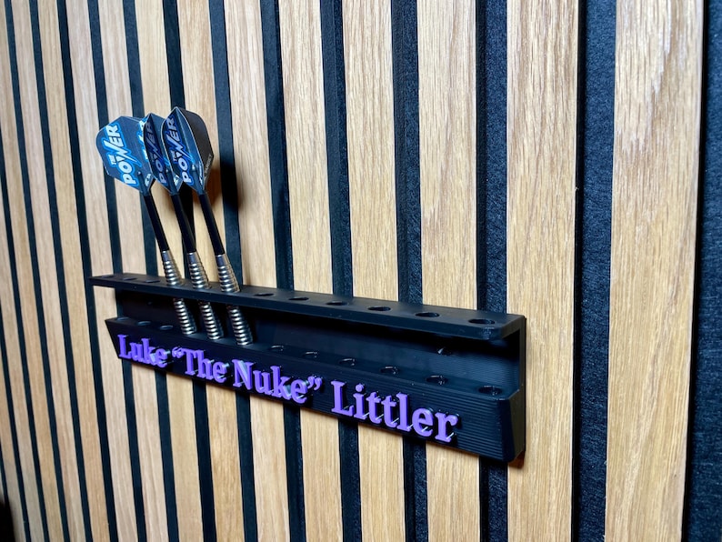 Puede incluir: Soporte negro para dardos con tres dardos. Los dardos tienen ca&ntilde;as negras y plumas Power azules y blancas. El soporte tiene el texto "Luke "The Nuke" Littler" en morado.