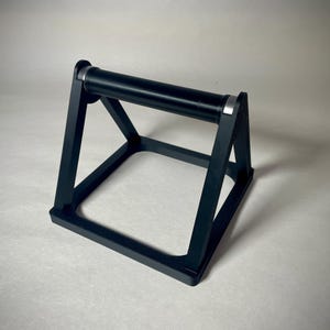 May include: Black push-up bar with a rectangular base and a cylindrical handle. The bar has a sturdy, geometric design with silver accents on the handle. This fitness equipment is designed to assist with push-up exercises.