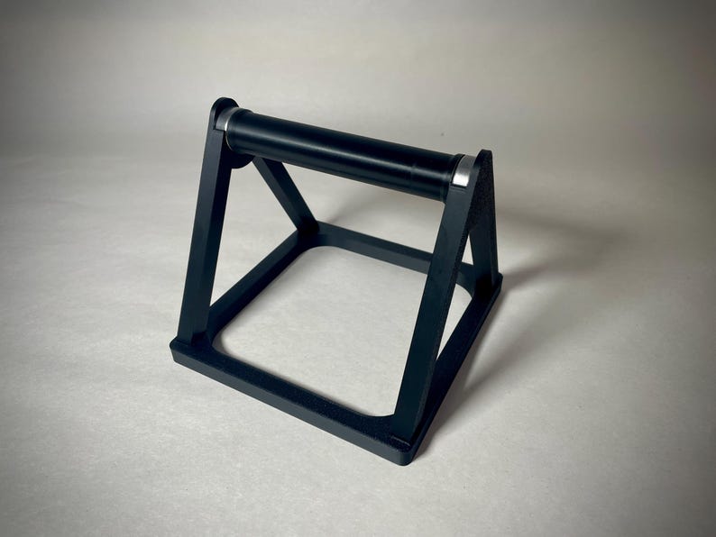 May include: Black push-up bar with a rectangular base and a cylindrical handle. The bar has a sturdy, geometric design with silver accents on the handle. This fitness equipment is designed to assist with push-up exercises.