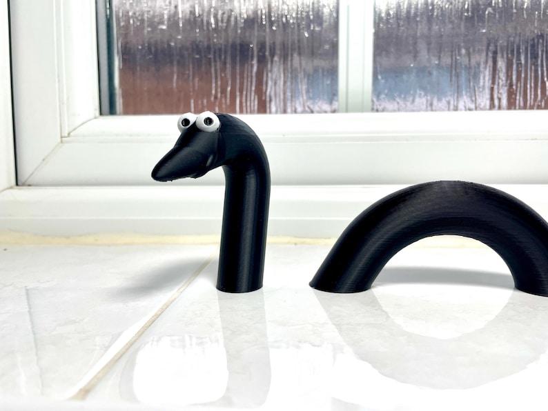 May include: A black, 3D printed, snake-like toy with googly eyes. The toy is in two pieces, with the head and neck separate from the body.