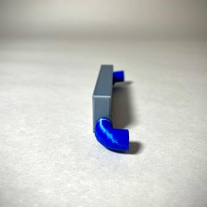 May include: A gray rectangular object with two blue, curved, tube-like extensions. The object is set against a neutral background. The blue extensions are at right angles to the main body of the object.