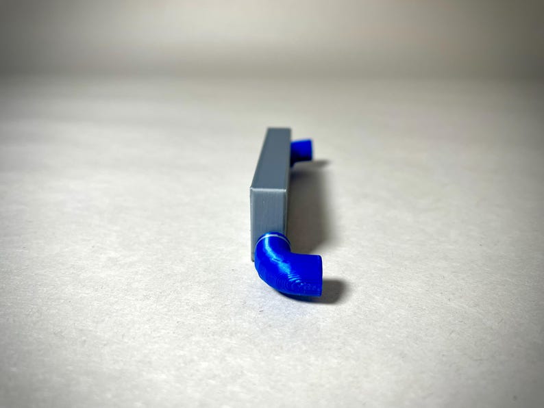 May include: A gray rectangular object with two blue, curved, tube-like extensions. The object is set against a neutral background. The blue extensions are at right angles to the main body of the object.