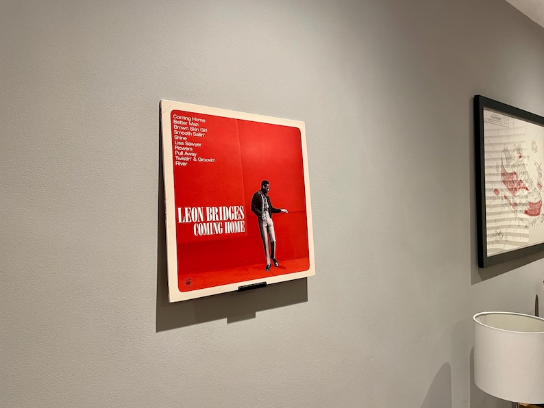 May include: A red vinyl record album cover with a black and white photo of a man in a suit and tie. The album is titled "Leon Bridges Coming Home" and lists the songs "Coming Home", "Better Man", "Brown Skin Girl", "Smooth Sailin", "Shine", "Lisa Sawyer", "Flowers", "Pull Away", "Twistin' & Groovin", "River".