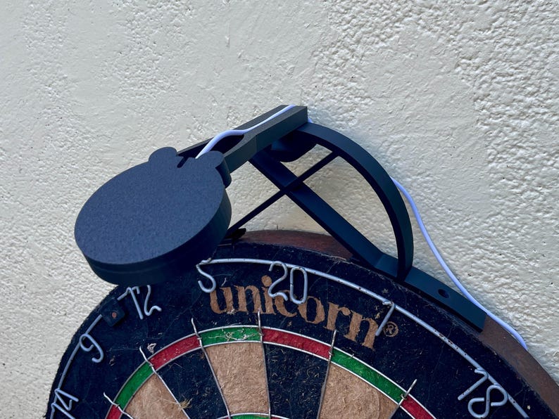 Dart board with attached lamp on the top. The lamp extends out in front of the board in order to cast light on the play area. Lamp is black modern design with a puck light at the end.