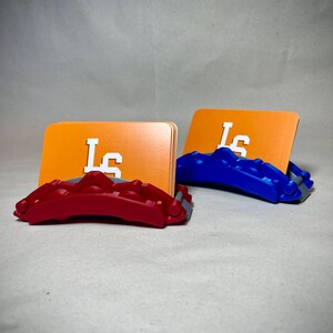 May include: Two card holders, one red and one blue, each supporting an orange card with the white letters "LS". The holders have a textured design. The background is a neutral gray.