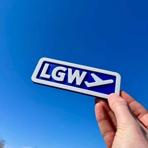 May include: A blue and white sign with the letters LGW and a white airplane symbol pointing to the right.