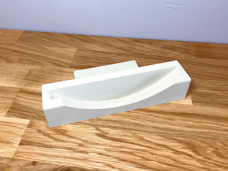 May include: White plastic phone stand with a curved, indented area for holding a phone.