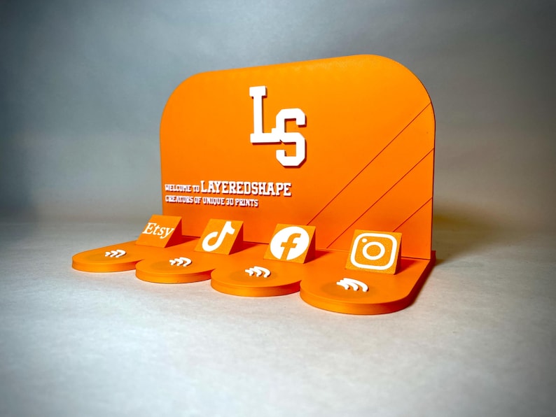 May include: An orange display stand with the text "LS" and "LAYEREDSHAPE" in white. The stand features platforms with Etsy, TikTok, Facebook, and Instagram logos. The design is made of 3D printed material.