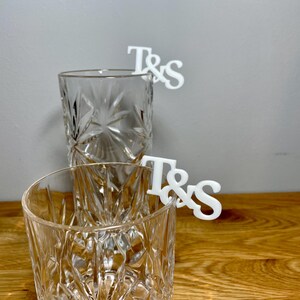 Tumbler and tall glass with a set of initial letters clipped onto the side. Drink topper is white and the photo shows a grey background.