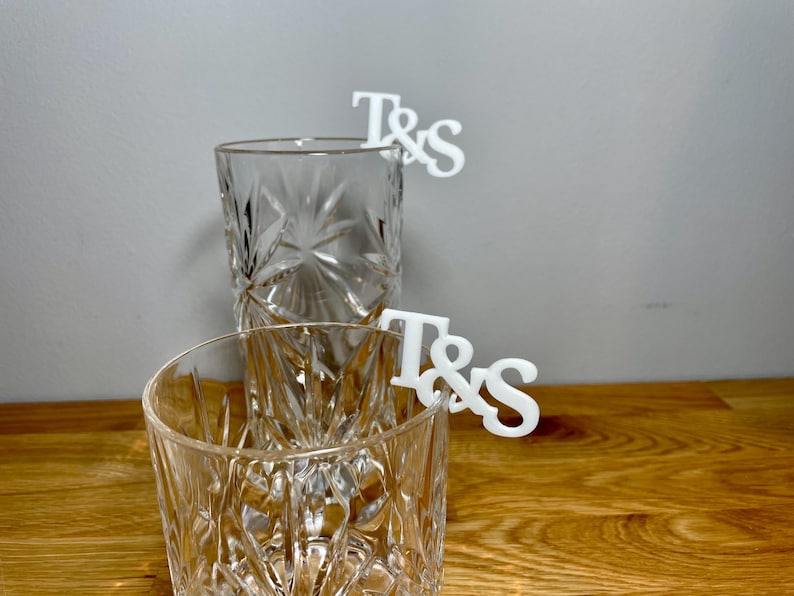 Tumbler and tall glass with a set of initial letters clipped onto the side. Drink topper is white and the photo shows a grey background.