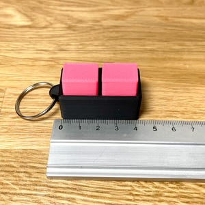 May include: A black keychain with a pink eraser on each side. The keychain is about 4 inches long.