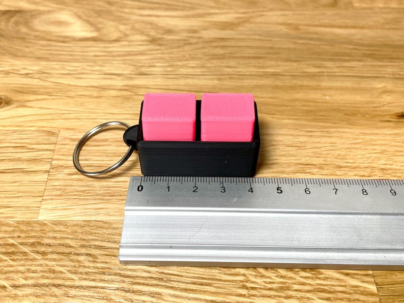 May include: A black keychain with a pink eraser on each side. The keychain is about 4 inches long.