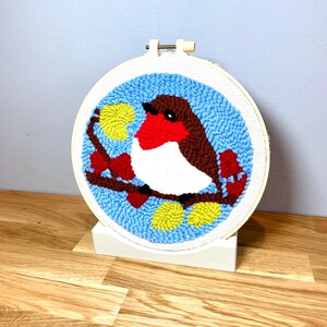 May include: A hand-stitched embroidery hoop with a blue background and a red-breasted robin perched on a branch with yellow leaves. The robin is brown, white, and red.