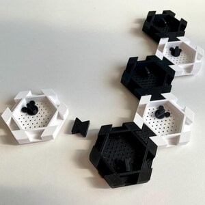 May include: A collection of black and white hexagonal containers with a Mickey Mouse head design in the center. The containers are arranged on a white surface. Some containers are black, others are white.