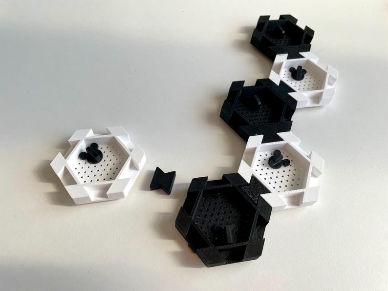 May include: A collection of black and white hexagonal containers with a Mickey Mouse head design in the center. The containers are arranged on a white surface. Some containers are black, others are white.