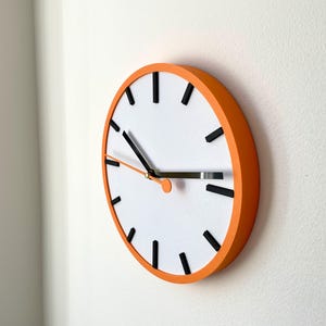 May include: A round orange clock with black hour and minute hands and black markings for the hours. The clock face is white.