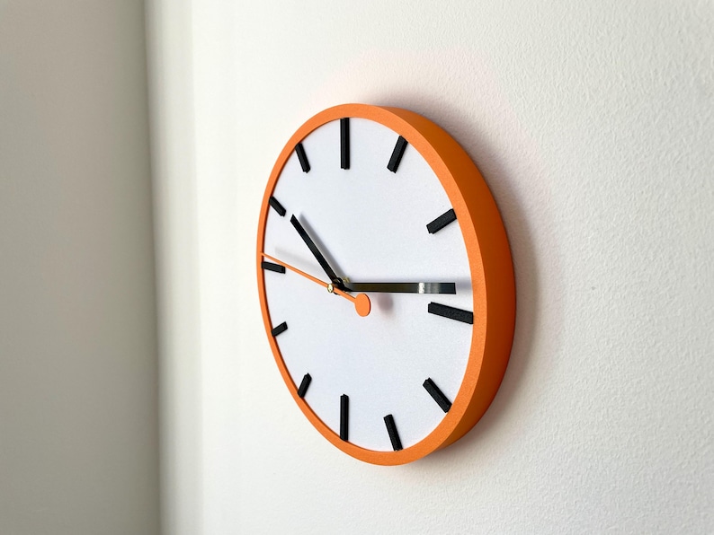 May include: A round orange clock with black hour and minute hands and black markings for the hours. The clock face is white.