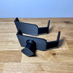 May include: Two black plastic camera mounts with a threaded hole for a tripod. The mounts are designed to be attached to a surface.